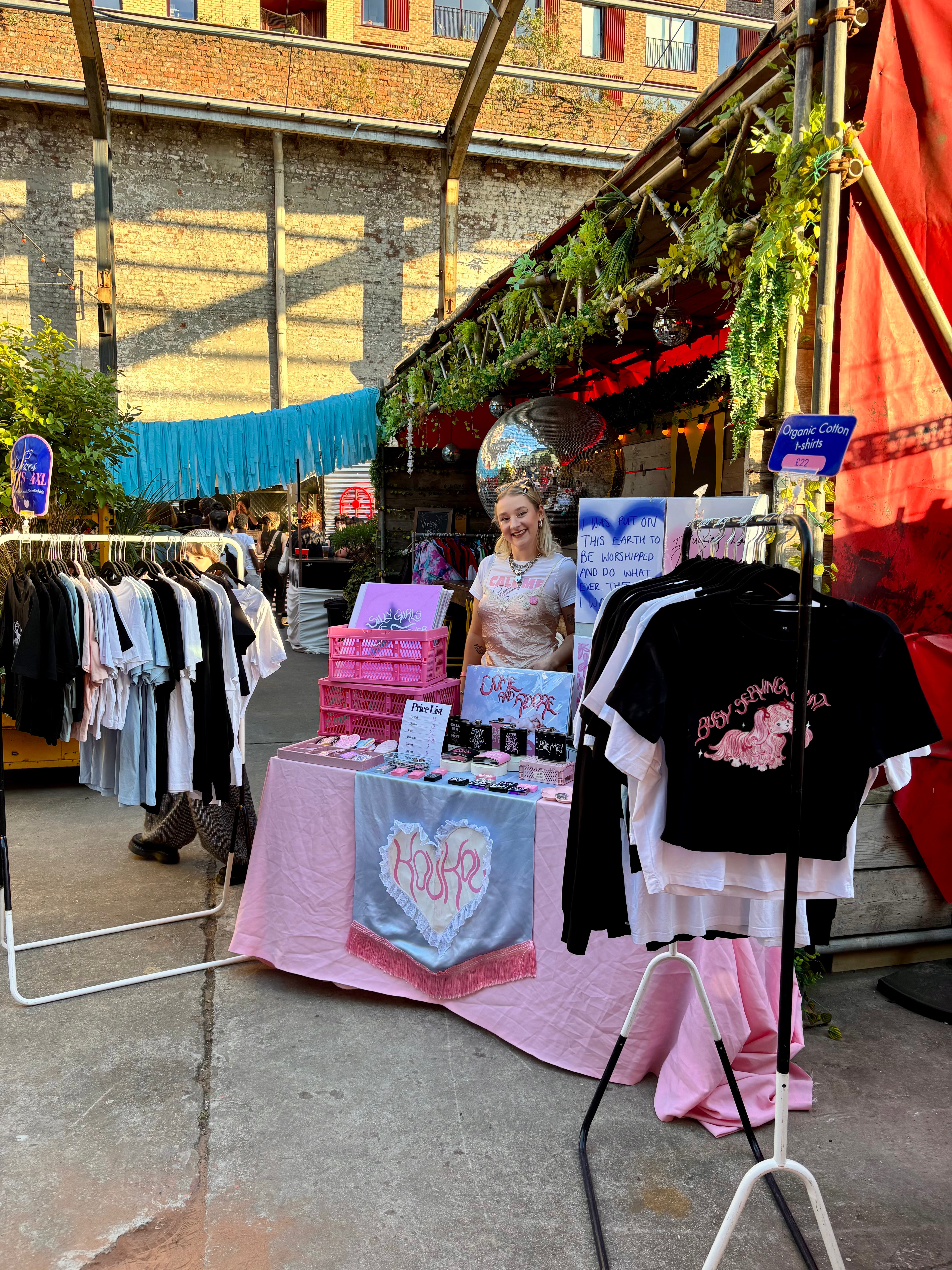 Outdoor market scene with vendors and clothing displays.