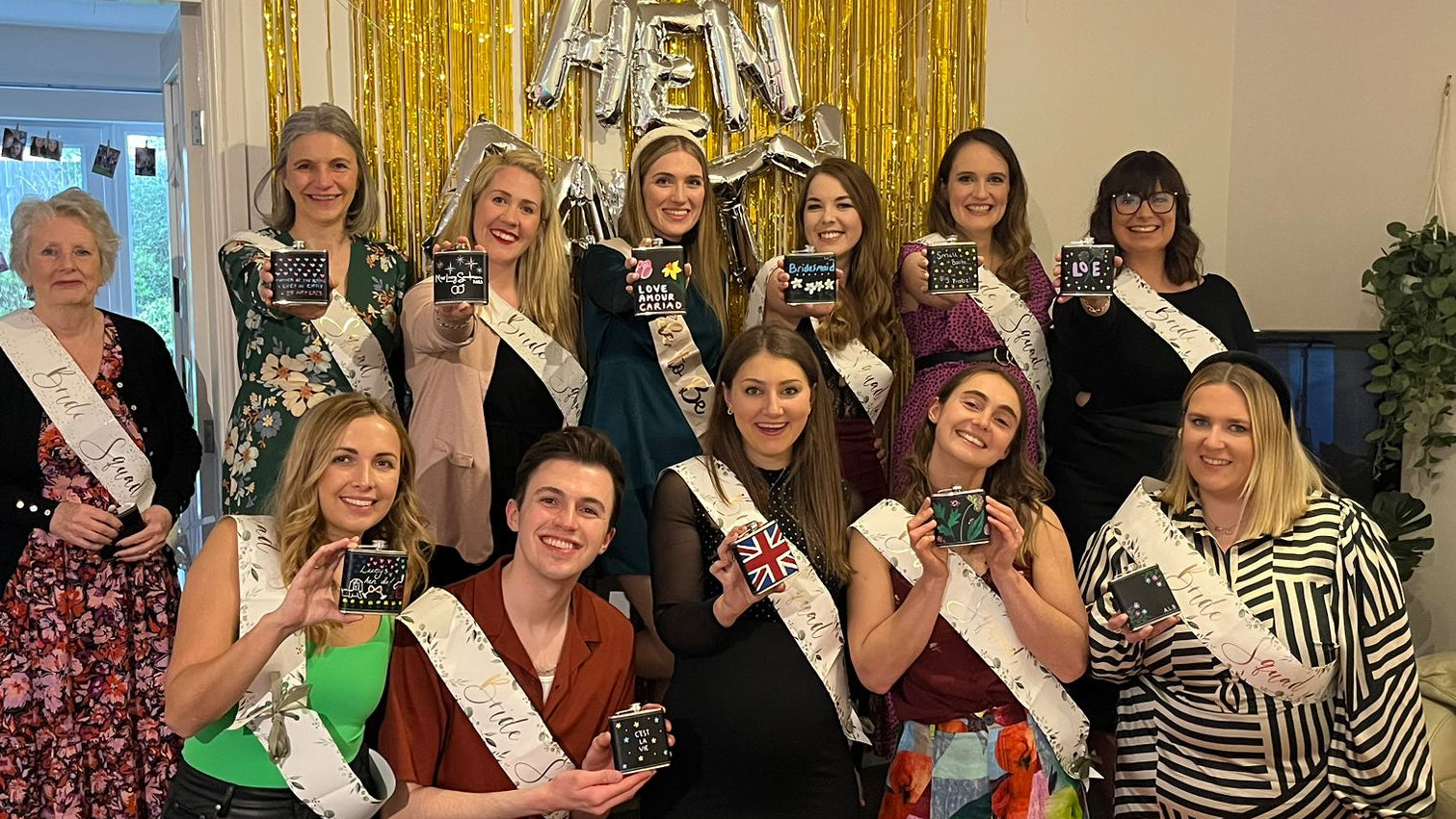 Group of women posing together in a room with decorative hen do sashes and signs.